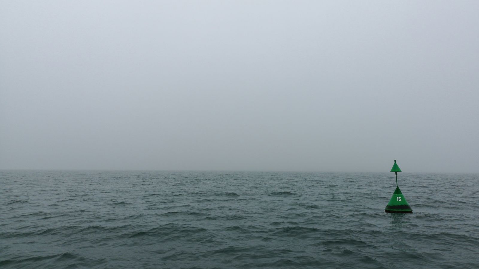 A green channel buoy in fog on open water