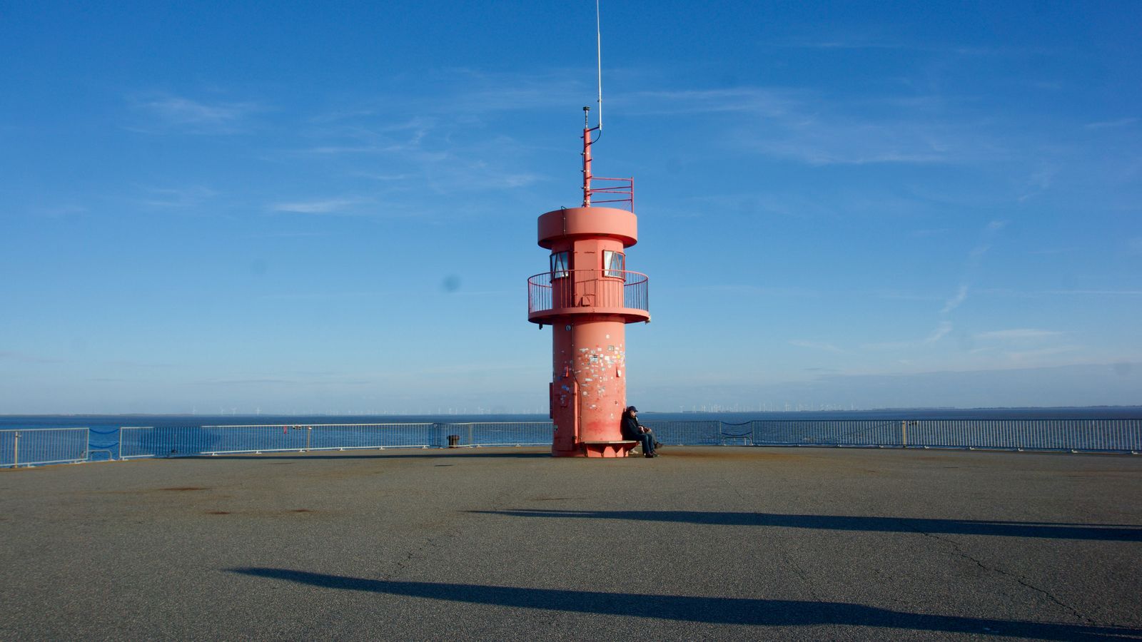 A red steel radio tower carrying antennas on a rocky shoreline