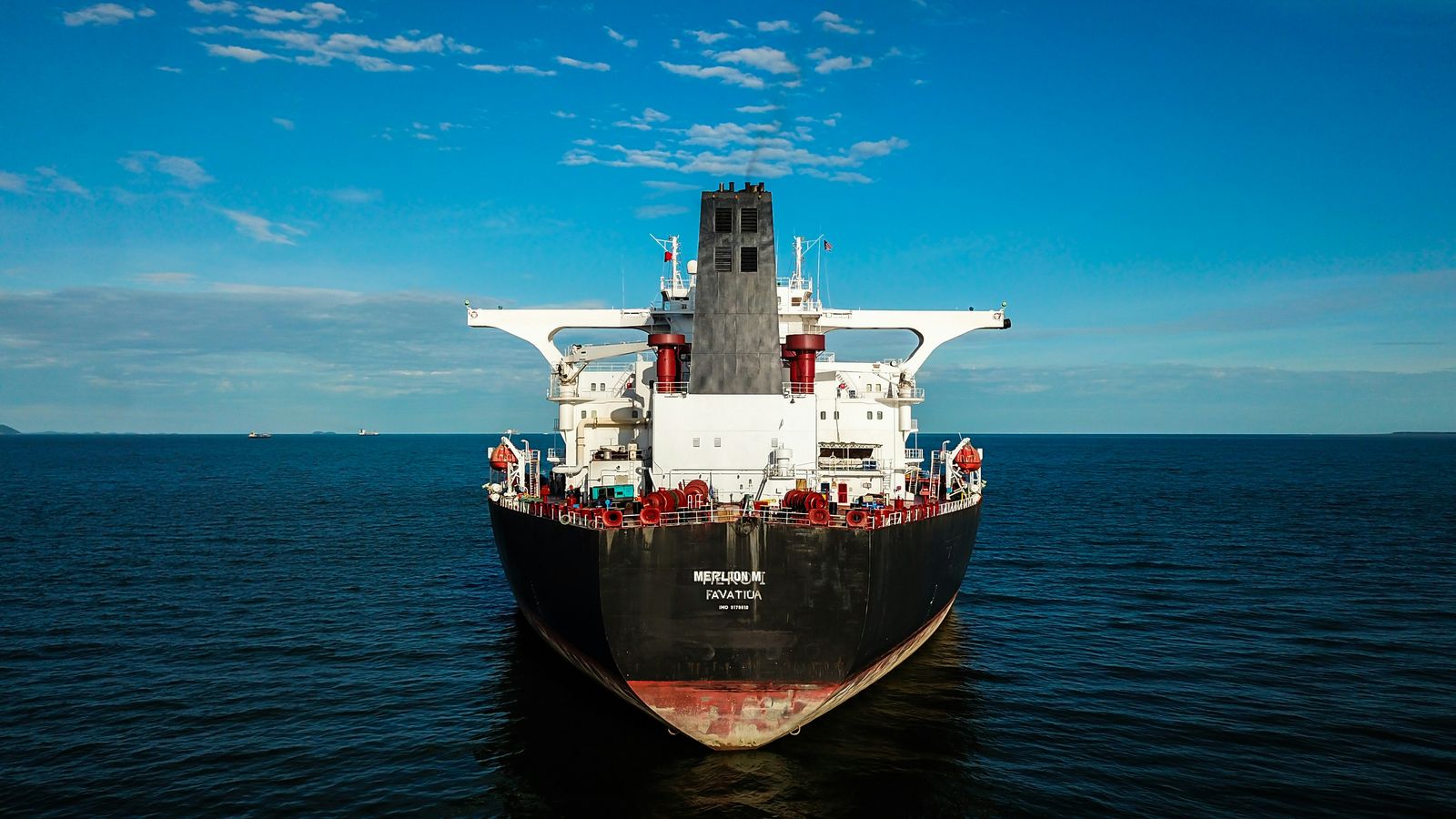 A red and black cargo ship under way with deck cranes on a clear day