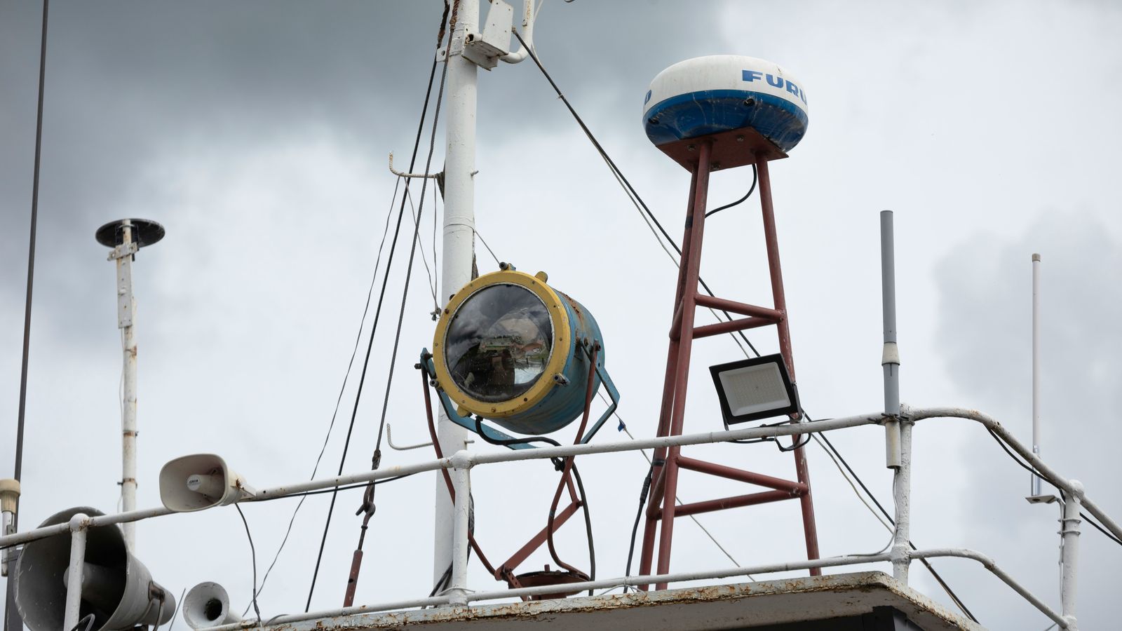 A vessel's mast carrying a radar dome, a searchlight and VHF whip antennas