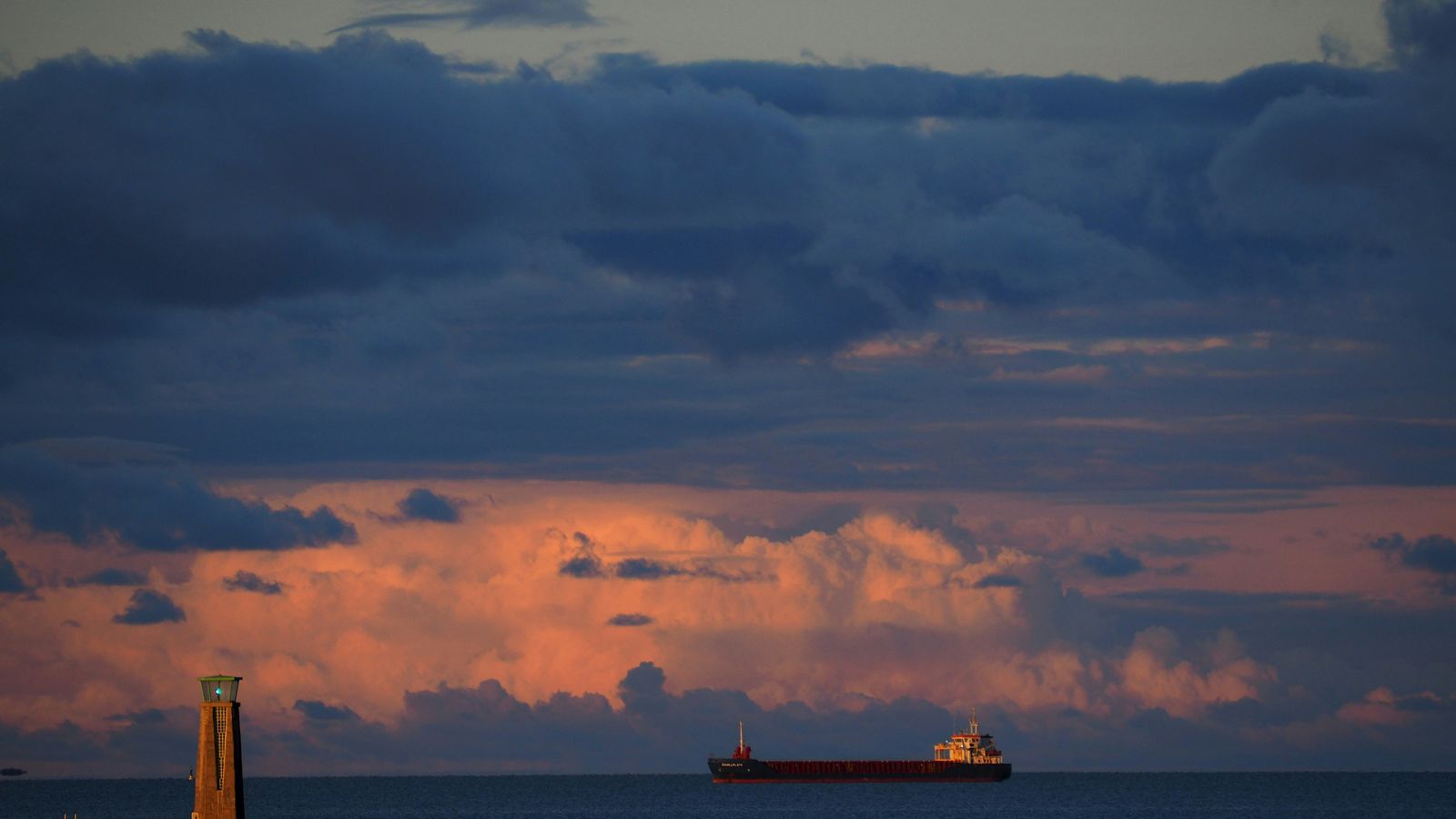 A cargo ship on the horizon beyond a lighthouse
